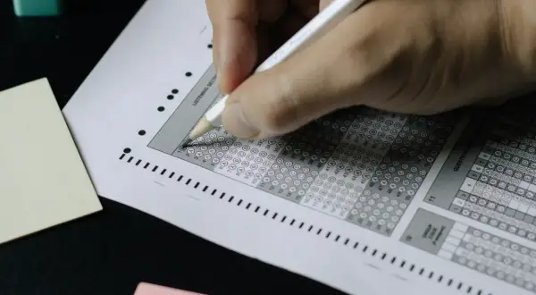 Ręka z ołówkiem zaznacza odpowiedzi na arkuszu testowym. To są skrzyżowania testy z odpowiedziami.