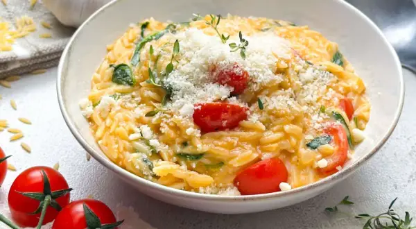Schüssel mit Orzotto, Tomaten, Spinat und Parmesan, garniert mit Thymian.