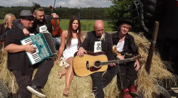 Zespół muzyczny siedzi na sianie, grając na akordeonie, skrzypcach i gitarze. Ich muzyka to hołd dla Ukrainy, śpiewają podaj rękę Ukrainie.