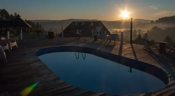 Poranek nad basenem z widokiem na Bieszczady. Słońce wschodzi nad mglistymi dolinami, tworząc magiczną atmosferę. Idealne miejsce na relaks w **termy Bieszczady**.