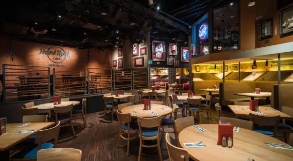 Wnętrze Hard Rock Cafe Warszawa. Drewniane stoły i krzesła, ściany ozdobione pamiątkami muzycznymi i neonem "Rock Radio".