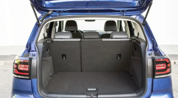 Błękitny Volkswagen T-Cross z otwartym bagażnikiem. Widać tylne siedzenia i przestronną przestrzeń bagażową, idealną na wakacyjne wyjazdy.