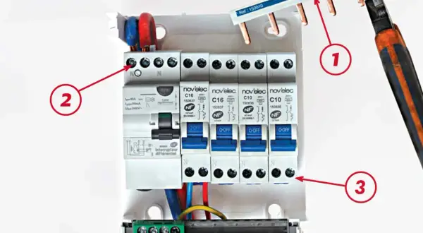 Un tableau électrique avec un interrupteur différentiel et des disjoncteurs. Le câblage est en cours, avec des fils rouges, bleus et jaunes.