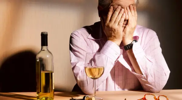 Mann mit Händen vor dem Gesicht, Wein, Korkenzieher und Brille auf dem Tisch. Möglicherweise ein Hinweis auf Korsakow-Demenz.