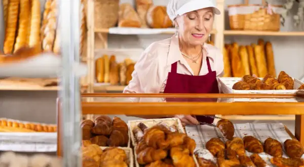 Starsza pani piekarz z uśmiechem układa świeże croissanty. To ulga dla pracujących seniorów, którzy wciąż mają pasję.