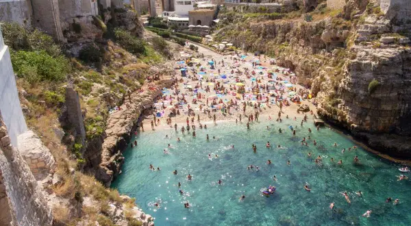 Spiaggia affollata e mare cristallino a Polignano a Mare. Perfetto per scoprire cosa fare in questa perla pugliese: nuotare, prendere il sole e godersi la vista.