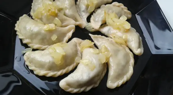 Pyszne pierogi z płuckami, polane skarmelizowaną cebulką, kuszą na czarnym talerzu.