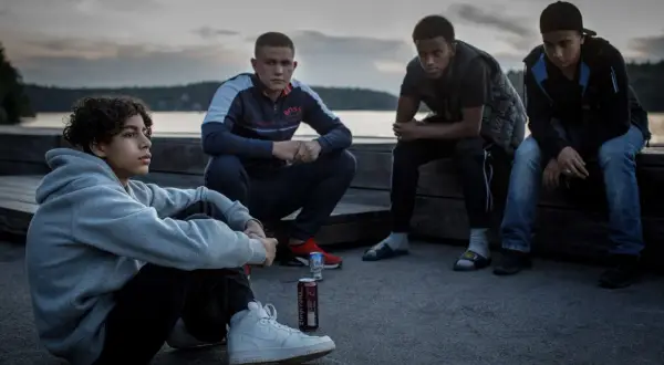 Fyra unga män sitter vid vattnet i skymningen, en scen från filmen Vinterviken (2021).