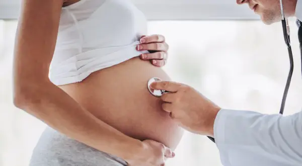 Lekarz osłuchuje brzuch ciężarnej kobiety, która jest w 24 tygodniu ciąży. Słychać bicie serca dziecka.