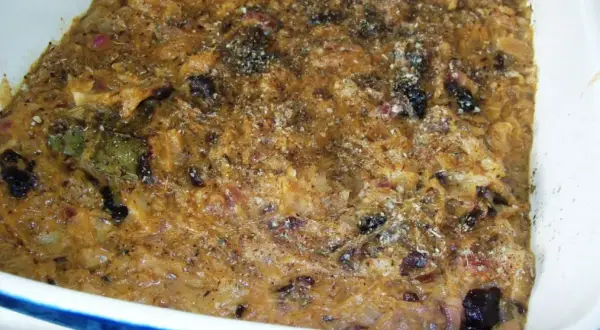 Schab po góralsku w naczyniu, z widocznymi kawałkami mięsa, cebuli i suszonych śliwek, posypany przyprawami.