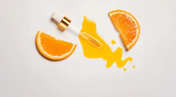 Ein Pipettenfläschchen tropft ein leuchtendes Serum neben Orangenscheiben. Vitamin C für das Gesicht, das für strahlende Haut sorgt.