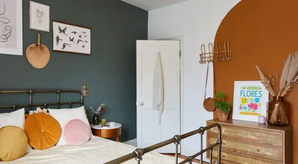 A cozy bedroom with a dark green accent wall, white door, and a terracotta arch. This space shows how to make a small bedroom look bigger with light bedding and strategic decor.