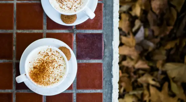 Två koppar med krämig pumpkin spice latte, toppade med kanel och en pepparkaka. Perfekt för ett mysigt pumpkin spice latte recept.