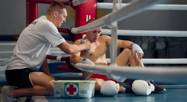 A trainer tends to a boxer in a ring, applying ice to his chest. This shows one aspect of how boxing works: the physical toll and the need for recovery.
