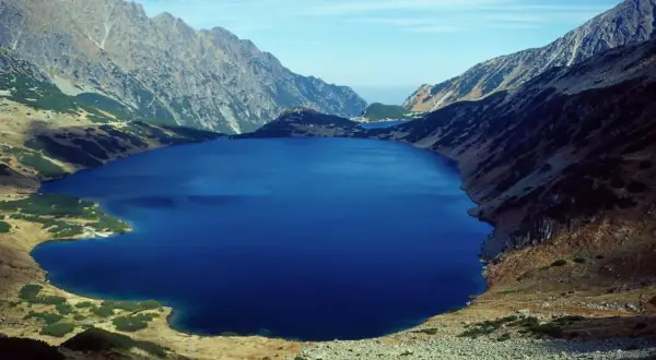 Głębokie, granatowe jezioro otoczone skalistymi zboczami i trawami. Widok na malownicze doliny w Tatrach.