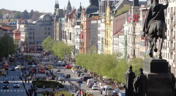 Pomnik konny na placu Wacława w Pradze, z widokiem na tętniącą życiem ulicę pełną ludzi i samochodów.
