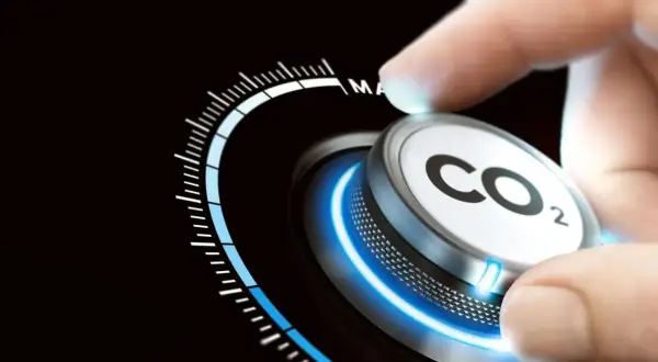 Dłoń obraca pokrętło z napisem CO2, zmniejszając emisje. Skala wskazuje na redukcję.