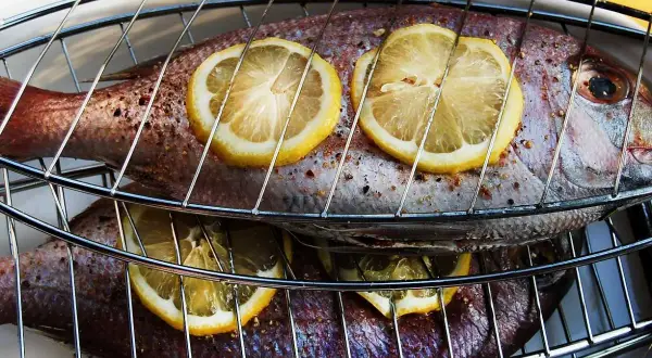 Två hela fiskar ligger på ett grillgaller, toppade med citronskivor. Snart är det dags att grilla fisk!