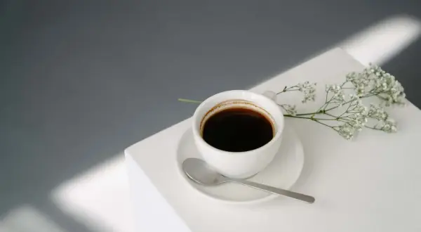 En vit kaffekopp med en sked och en liten blomsterkvist. Kanske inte det bästa valet om man är dålig i magen av kaffe på morgonen.