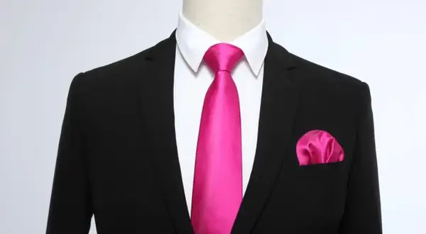 Un completo nero con camicia bianca, una cravatta rosa acceso e un fazzoletto da taschino coordinato. Un abbinamento audace e di classe.