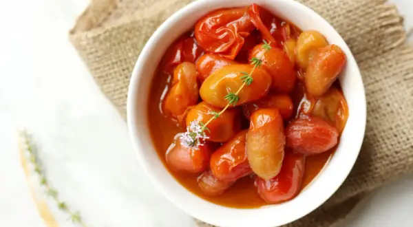 Deliciosos tomates cherry confitados en un cuenco blanco, adornados con tomillo fresco y una flor morada.