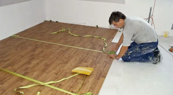 Układanie paneli podłogowych w mieszkaniu 50m2. Remont trwa, a wykonawca precyzyjnie dopasowuje deski.