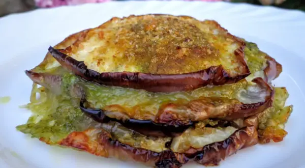 Tramezzini con melanzane grigliate, pesto e formaggio fuso, un'esplosione di sapori mediterranei su un piatto bianco.