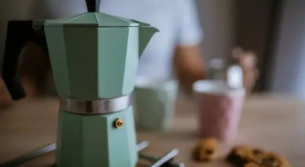 Moka verde pronta per il caffè, ma forse manca qualcosa per capire perche la moka non fa il caffe. Biscotti e tazze sullo sfondo.
