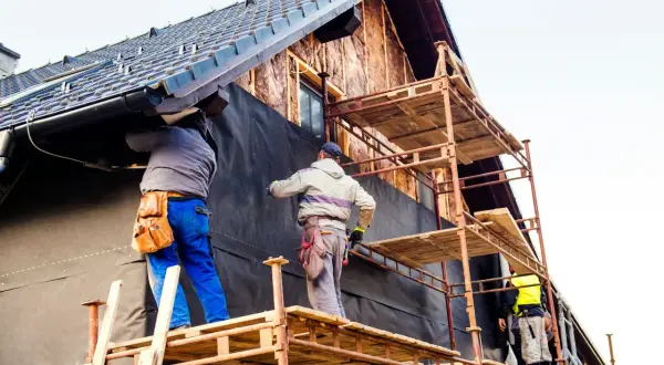 Trois ouvriers sur des échafaudages installent une membrane noire pour l'isolation extérieur, une aide précieuse pour l'efficacité énergétique.