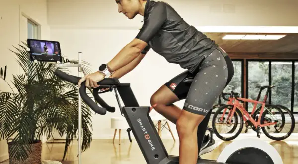 Mujer entrenando en bicicleta estática, ajustando su postura para un mejor rendimiento.