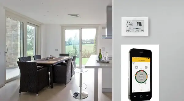 Termostato e cronotermostato: un confronto visivo. Un moderno soggiorno con tavolo da pranzo e un dispositivo di controllo della temperatura, accanto a uno smartphone che mostra un'app per la gestione della casa.