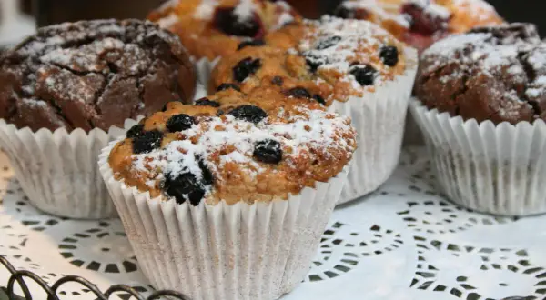 Flera saftiga muffins, några med blåbär och pudrade med florsocker, ligger på ett vackert fat.