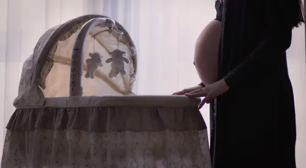Gravid kvinna med ruckbart huvud vid en vagga med nallar.