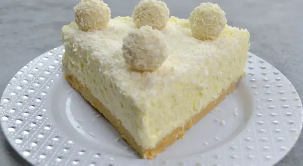 Pyszny sernik Rafaello, udekorowany wiórkami kokosowymi i kulkami przypominającymi Rafaello.