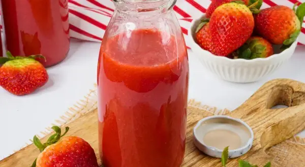 Frische Erdbeeren werden zu einem leckeren Smoothie verarbeitet. Eine Flasche mit dem roten Fruchtgetränk steht bereit.