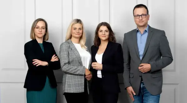 Cztery osoby w strojach biznesowych stoją przed jasną ścianą.