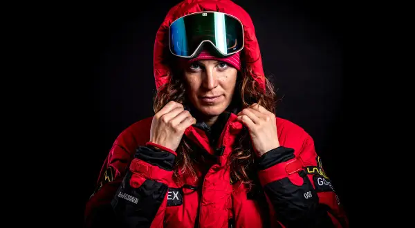 Tamara Lunger, bereit für extreme Bedingungen, zieht ihre rote Kapuze hoch. Ihre Skibrille spiegelt das Licht.