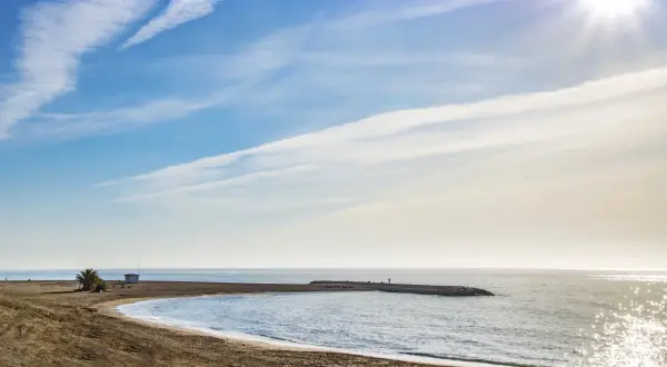 Playa de Macenas en Almería, con un muelle y el sol brillando en el mar.
