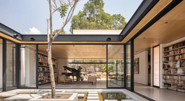 Modernas casas con patio interior central, un árbol solitario y un estanque de agua reflejan la luz natural.