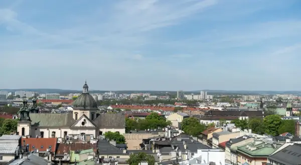 Widok na krakowskie dachy i kościół z kopułą. W tle nowoczesne budynki, które mogą wpływać na ceny mieszkań w Krakowie za m2.