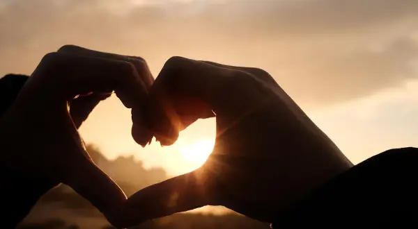 Dłonie tworzą serce na tle zachodzącego słońca. Początek pięknej historii, która może być jak love bombing.