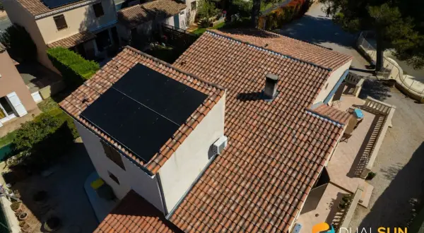 Toits de maisons avec panneaux solaires noirs. Une unité extérieure de pompe à chaleur est visible sur le mur.