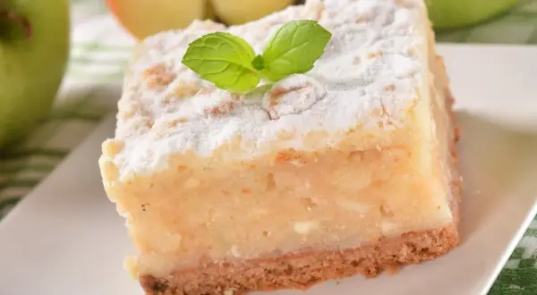 Pyszne, ekspresowe ciasto z jabłkami, posypane cukrem pudrem i udekorowane listkiem mięty. Idealne na szybki deser.