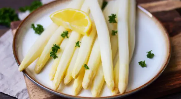 Frischer weißer Spargel, perfekt gegart, mit Zitrone und Petersilie garniert. Ein Genuss, wenn Spargel kochen auf dem Tisch steht.