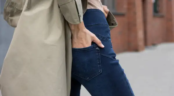 Kobieta w beżowym płaszczu i granatowych jeansach bootcut, które delikatnie rozszerzają się ku dołowi.
