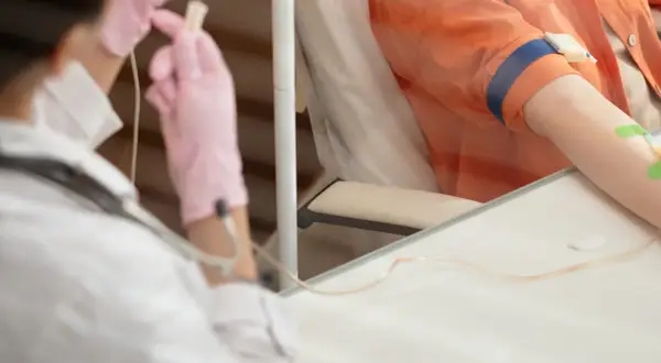 Pierwsza chemioterapia: pielęgniarka w różowych rękawiczkach przygotowuje kroplówkę dla pacjenta.