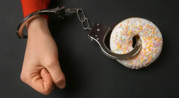Ręka w kajdankach, połączona z pączkiem. Symbol walki z uzależnieniem od słodyczy.