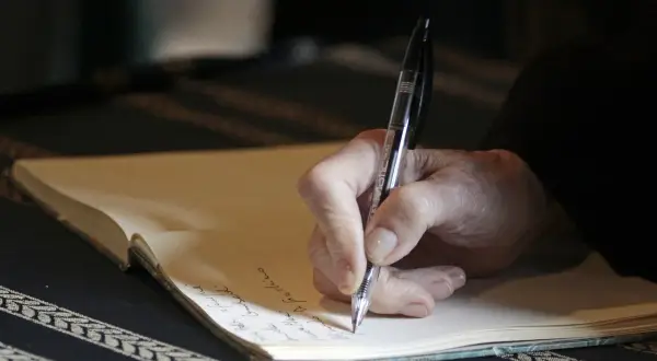 Mano che scrive su un quaderno, un momento intimo che ricorda l'apertura di un testamento olografo.