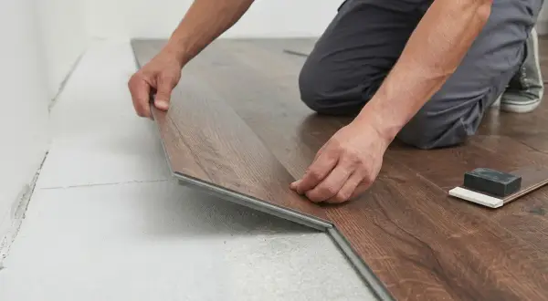 Installazione di una nuova posa pavimento spc effetto legno. Le mani esperte assemblano le doghe con precisione.