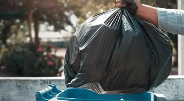 Mano depositando bolsa de basura en contenedor azul. ¿Quién paga la tasa de basura en un alquiler?